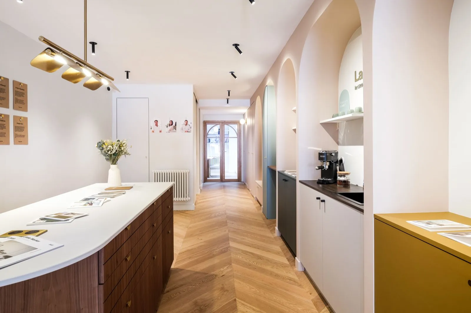 La cuisine vue depuis l'entrée : îlot, suspension dorée et portraits de l'équipe — Passage de Lyon
