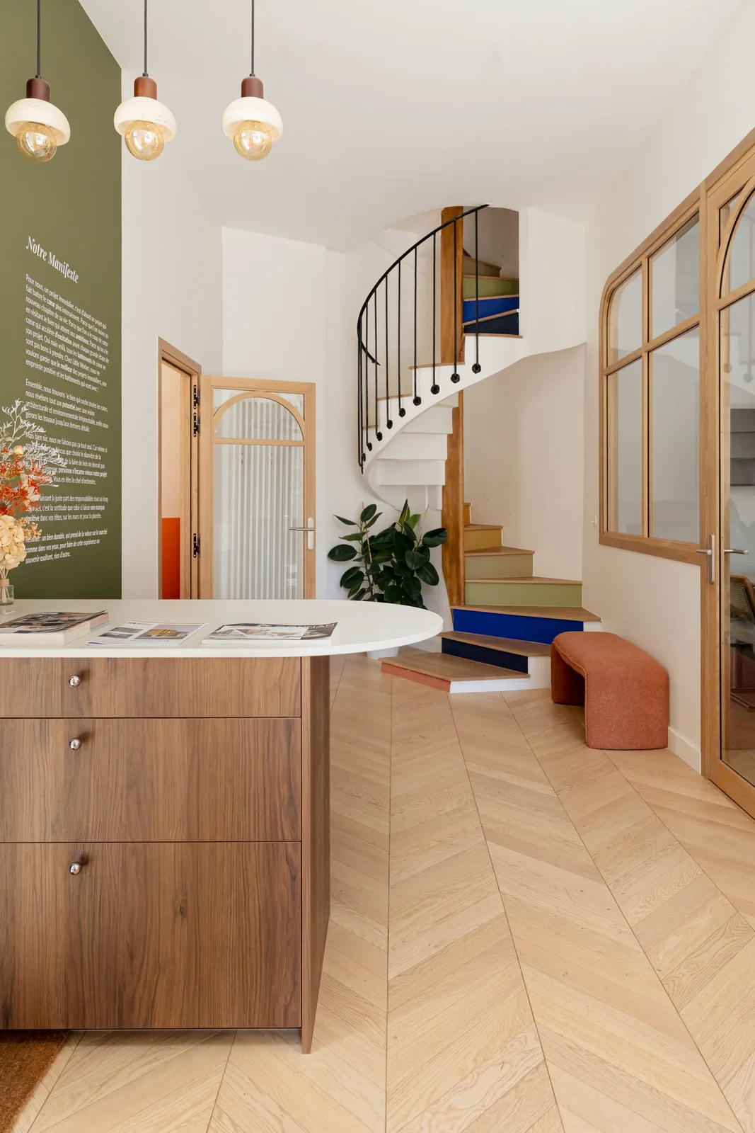 Accueil du Passage de Nantes : comptoir en noyer, mur manifeste vert, escalier hélicoïdal aux marches colorées et parquet à chevrons — Le Passage de Nantes