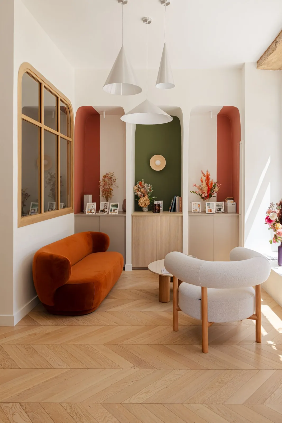 Salon d'accueil : canapé arrondi en velours terracotta, alcôves cannelées, miroir arqué et suspensions coniques — Le Passage de Nantes
